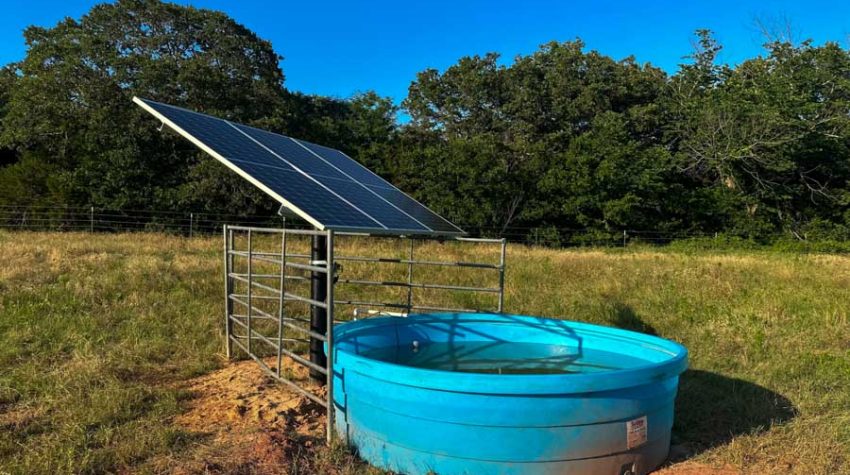 Solar-powered livestock watering system with blue tank in a rural pasture, installed by M&M Water Well Service
