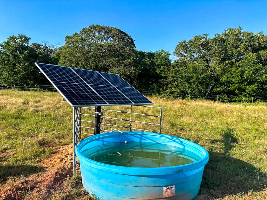 Solar-powered well pump system with a blue livestock watering tank in a rural Oklahoma pasture